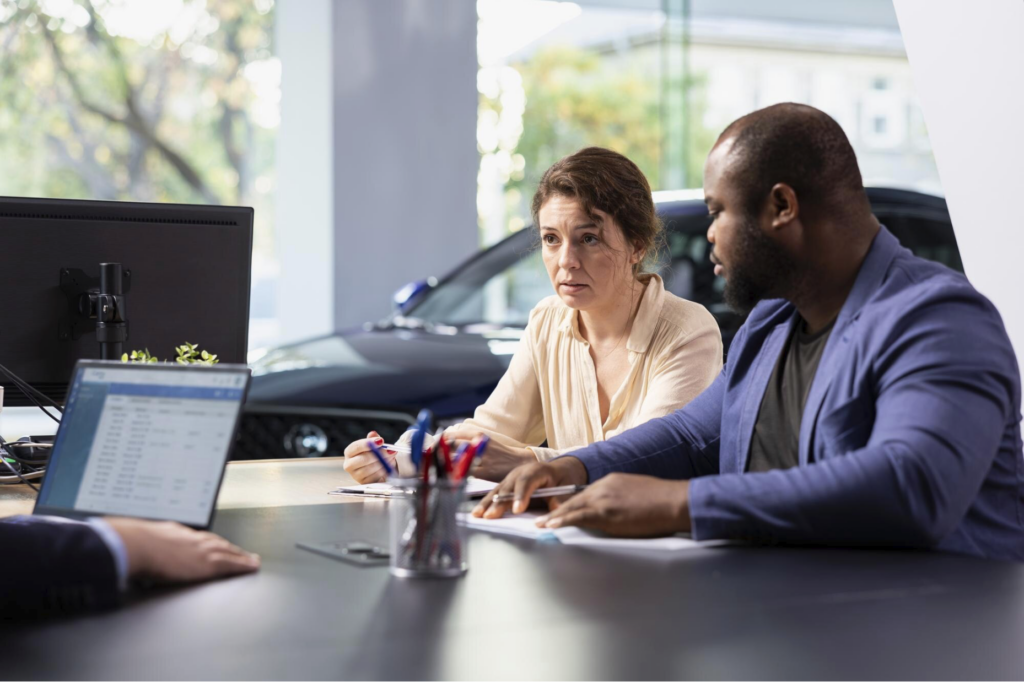 A couple sitting at a desk in a car dealership